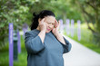 © Suzi Media  - Mature woman with a headache standing in the park with her fingers to her temples. Her eyes closed, she is suffering.