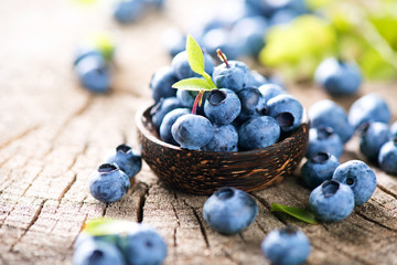 juicy and fresh blueberries with green leaves in wooden bowl