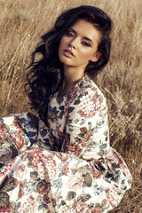 woman with dark hair wears luxurious colorful dress posing in summer field