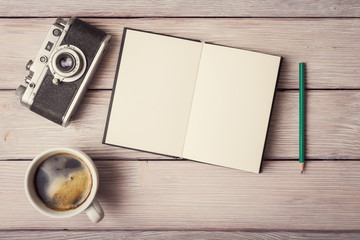 Retro camera, open memo book and cup of coffee on rustic wooden