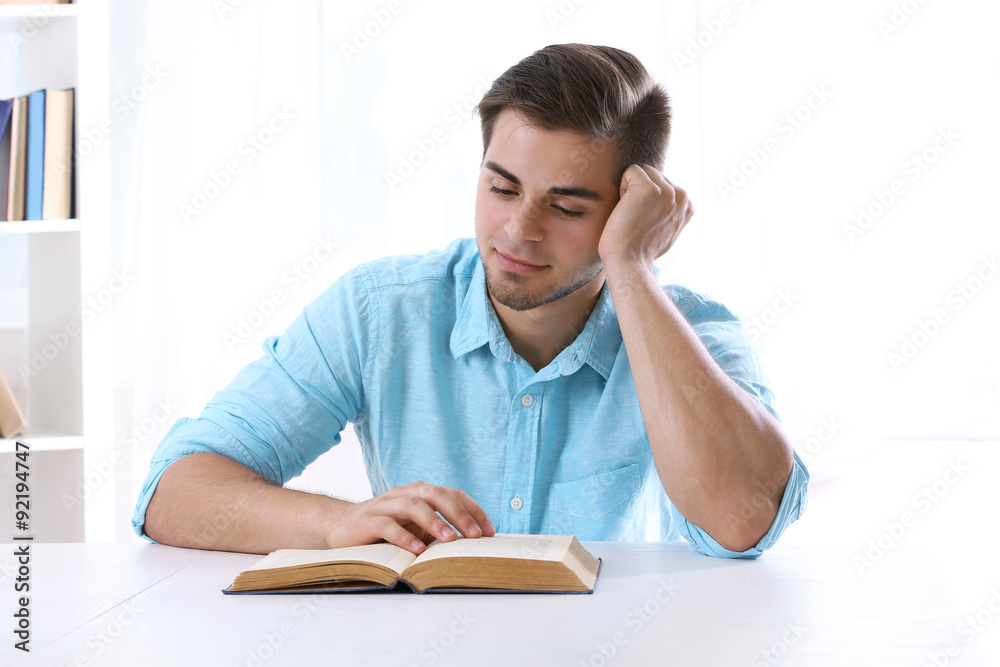 Young man reading book at table in room