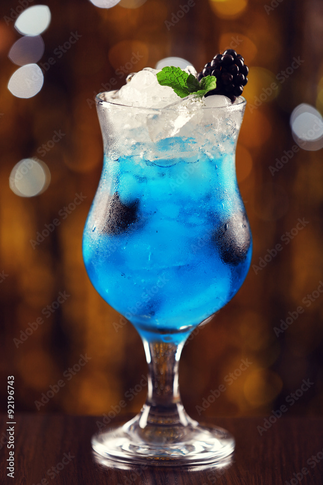 Glass of cocktail with ice on blurred lights background