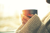 Fototapeta  - hands holding hot cup of coffee or tea in morning sunlight