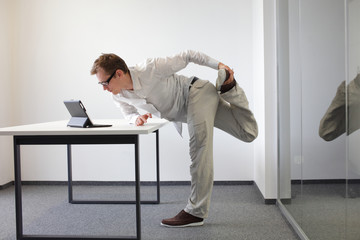 leg exercise during office work - standing man reading at tablet in his office