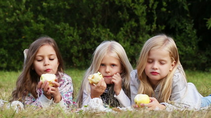 Wall Mural - Three girls eating apples in the park - habdheld shot