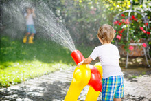 Two Little Kids Playing With Garden Hose In Summer