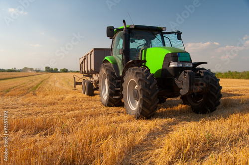 Foto Modern green tractor on agricultural field during harvest on sunny summer day