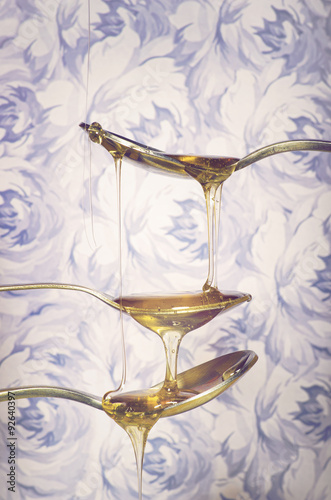 Nowoczesny obraz na płótnie Close up of bright honey dripping from spoons on flowers background.