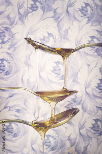 Naklejka nad blat kuchenny Close up of bright honey dripping from spoons on flowers background.