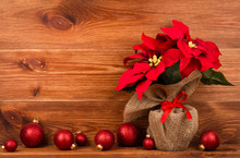 Christmas Decoration - Artificial Red Poincettia Flower Wrapped In Sackcloth With Red Balls On The Wooden Background.