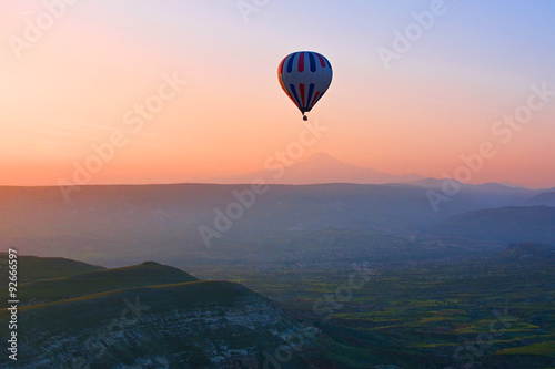 Fotografie, Obraz Hot air balloon flying over amazing landscape at sunrise, Cappad
