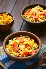 Wall Mural - Two rustic bowls of pasta salad made of tricolor fusilli, sweet corn, cucumber, cherry tomato and sausage, photographed with natural light (Selective Focus, Focus one third into the first salad)