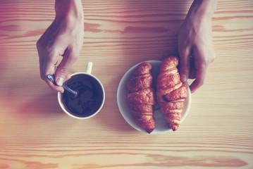 Wall Mural - Hands holding cup of coffee and croissants. View from above