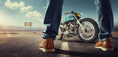 Wall Mural - Sport. Biker standing near the motorcycle on an empty road at sunny day. Close view on legs
