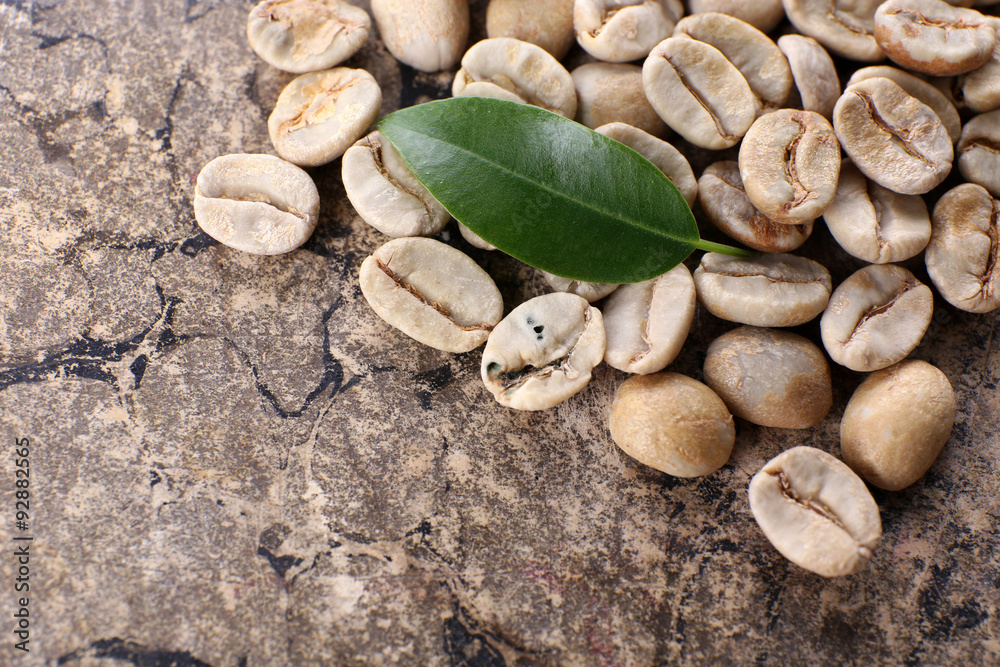Heap of green coffee beans with leaf on table close up