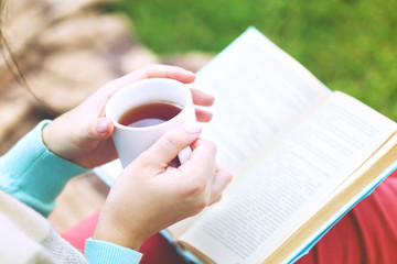 Wall Mural - Young woman with book sitting on green grass outdoors