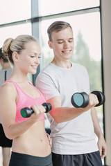 Poster - smiling young woman with personal trainer in gym