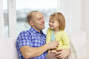 Wall Mural - happy father and daughter sitting on sofa at home