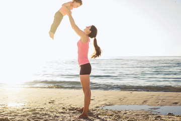 family workout - mother and daughter doing exercises on beach. H