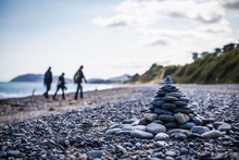 Stack Of Pebbles On Beach With Three People Walking In The Background