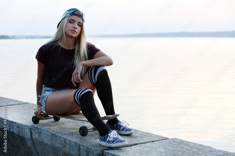 Young woman with skating board on the riverside