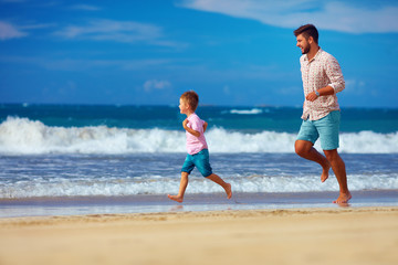 Wall Mural - happy excited father and son running on summer beach, enjoy life