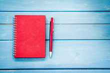 Red Notebook With Pen On Blue Wooden Table