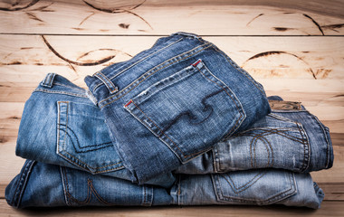 Sticker - fashionable clothes. pile of jeans on a wooden background