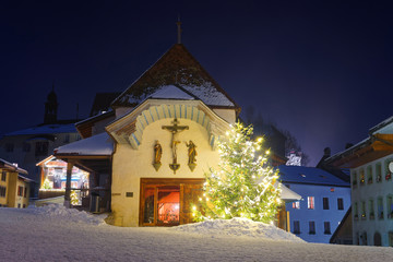 Wall Mural - Illuminated Christmas fir tree in front of the church in Gruyere