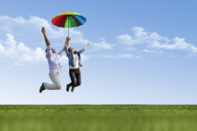 Happy Young Man And Girl Are Flying With Colorful Umbrella On Nature