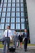© Westend61 - Team of business professionals walking out of office building with luggage