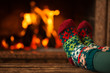 Feet in woollen socks by the Christmas fireplace. Woman relaxes by warm fire and warming up her feet in woollen socks. Close up on feet. Winter and Christmas holidays concept.