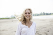 © Westend61 - Portrait of smiling blond woman with blowing hat on a beach