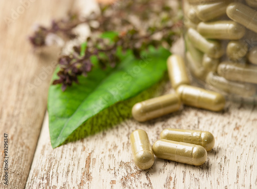 Fotografia Herb capsule with green herbal leaf on wood