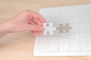 Female hand putting a missing piece into jigsaw puzzle