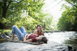 © Mint Images - A young man and woman lying on the rocks on a river bank.