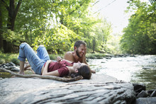 A Young Man And Woman Lying On The Rocks On A River Bank.