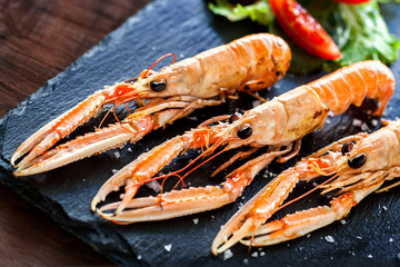 Wall Mural - Macro close up of fresh grilled crawfish platter with green salad served on elegant black tile.