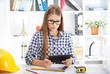© Stasique - Concentrated female architect with digital tablet studying construction plans. Young woman designer sitting at table with computer and engineering tools.