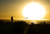 Fototapeta Kosmos - person flying toy plane over ocean with sun setting in the background