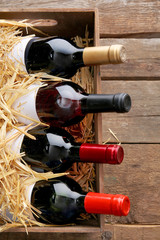 Poster - Box with straw and wine bottles on wooden background