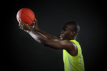 Wall Mural - African American basketball player holding ball on dark background