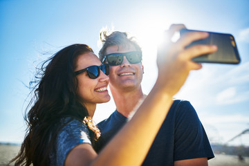 Wall Mural - smiling couple taking selfies with smartphone on the sunny beach
