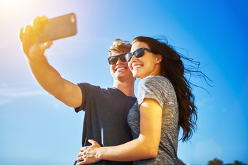 Wall Mural - couple selfie with lens flare on clear summer day and wearing sunglasses
