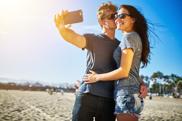 Wall Mural - attractive couple taking selfie under the intense sun on the beach together
