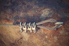 Solid Knot On Steel Rope. Iron Twisted Rope Fixed In Block By Screws Snap Hooks. Detail Of Rope End Anchored Into Sandstone Rock