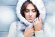 Beautiful young  brunette woman with eyes closed, wearing knitted sweater and fur hood, covered with snow flakes. Snowing winter beauty concept.