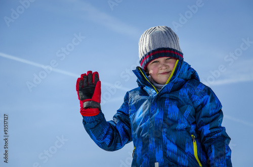 Photographie A child in winter clothes posing on a background of blue sky.
