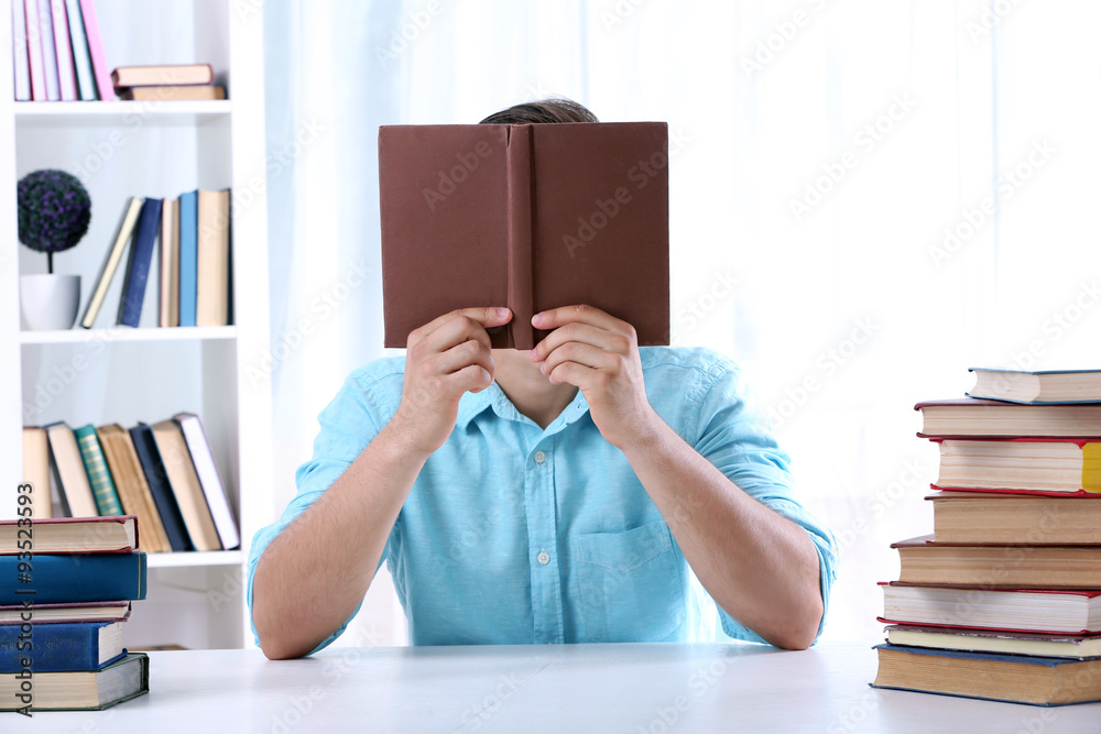Young man reading book at table in room