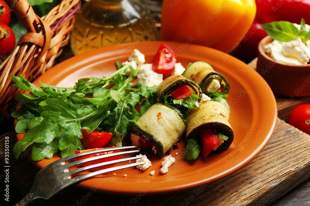 Zucchini rolls with cheese, bell peppers and arugula on plate, close-up, on table background